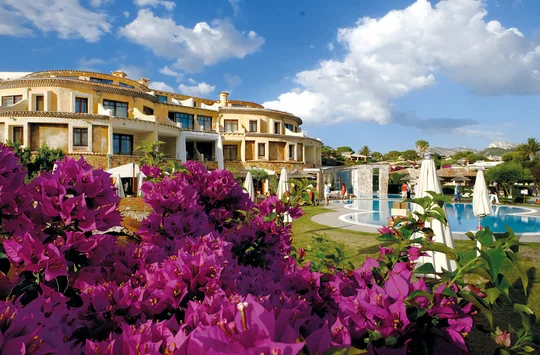 Das Hauptgebäude vom Hotel Baia Caddinas mit lila blühenden Blumen im Vordergrund