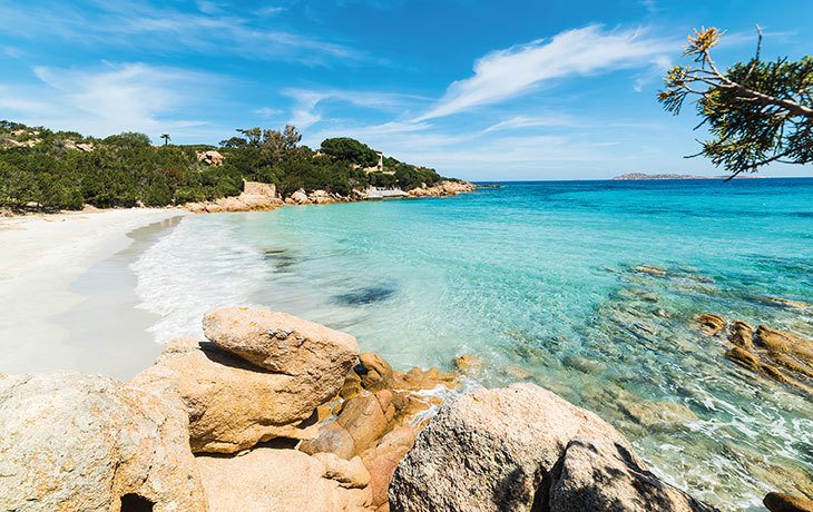 Heller Sand, blaues Meer und Granitfelsen an der Bucht Cappricioli auf Sardinien